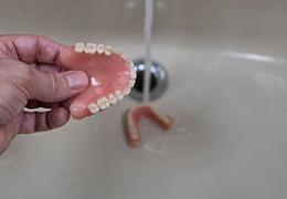 Person rinsing dentures in sink