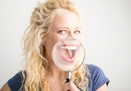 Woman holding magnifying glass up to her mouth, showing her dental implant restorations