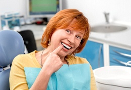 Happy dental patient pointing at her teeth, enjoying her dental implants