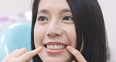 Woman pointing to her smile while sitting in dental chair