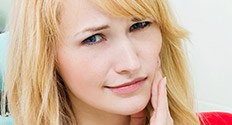 Woman in dental chair holding her jaw in pain