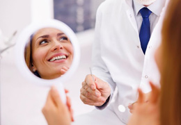 Dental patient holding mirror, looking at her dentist