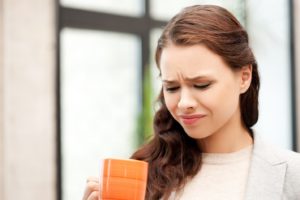 Woman sipping drink, frowning due to bad taste in mouth