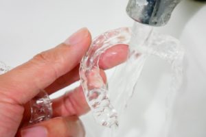 Hand rinsing SureSmile clear aligners under faucet after meal