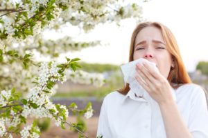 Woman standing next to tree, suffering from seasonal allergies