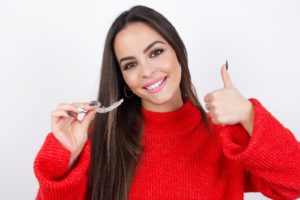 Woman in sweater giving thumbs up for clear aligners
