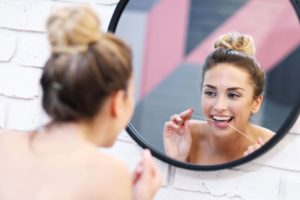 Smiling woman flossing in front of mirror